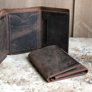 May include: Two brown leather wallets, one folded open to show the interior pockets and the other folded closed with the initials "AA" embossed on the front.