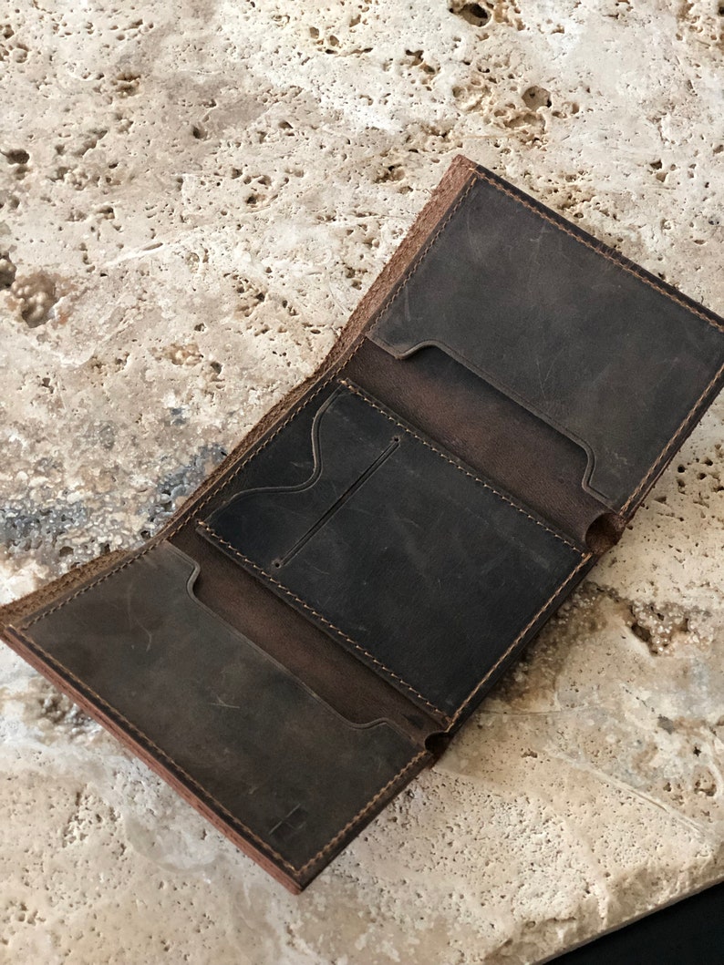May include: A brown leather wallet with multiple card slots and a billfold. The wallet is open and the interior is visible.