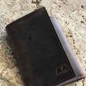 May include: A brown leather wallet with a stitched edge and the initials "AA" embossed on the front.
