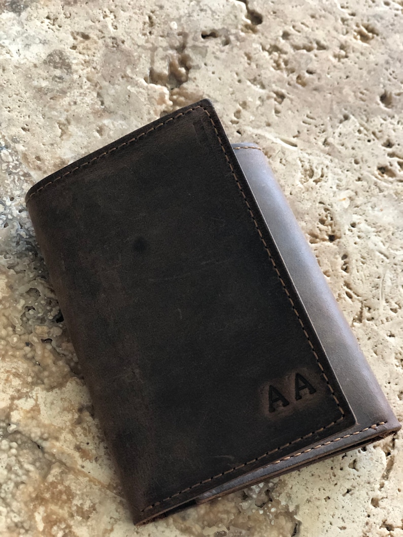 May include: A brown leather wallet with a stitched edge and the initials "AA" embossed on the front.