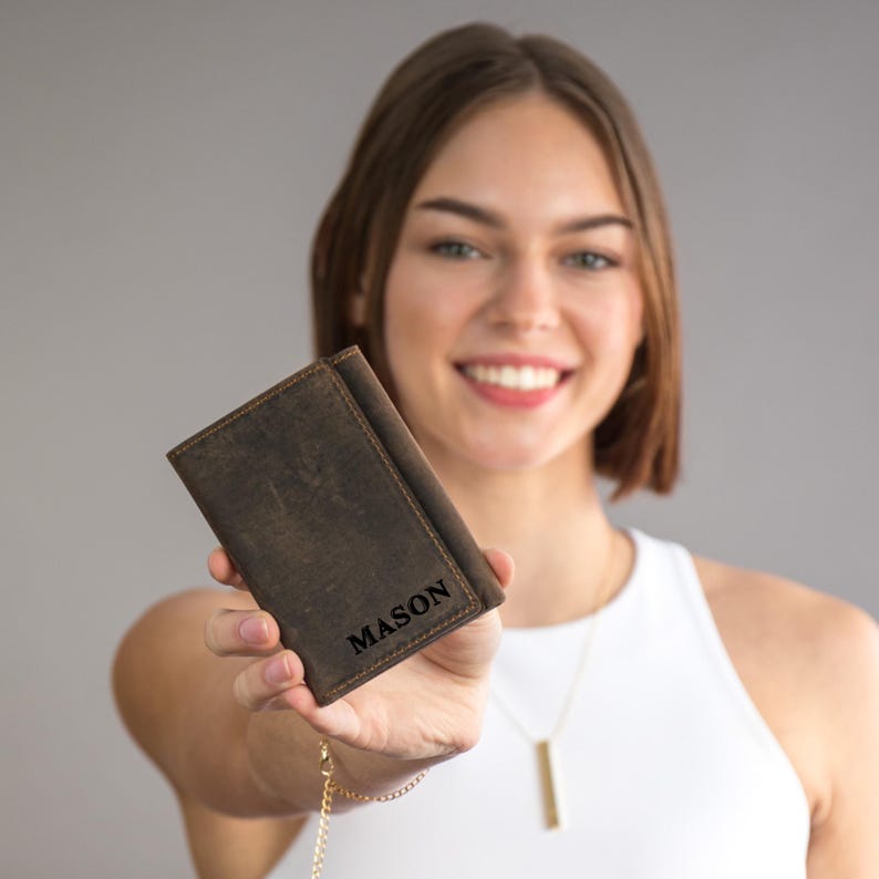 May include: A brown leather wallet with the name "MASON" embossed on the front. The wallet is being held by a person.