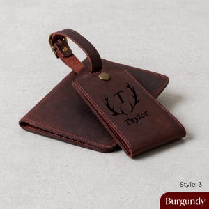 Puede incluir: Juego de etiqueta de equipaje y cartera de cuero burdeos. La etiqueta presenta un monograma con la letra "T" y el nombre "Taylor". La cartera y la etiqueta son de color burdeos oscuro con costuras rojas.