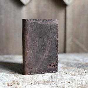 May include: A brown leather wallet with a stitched edge and the initials "AA" embossed on the front.