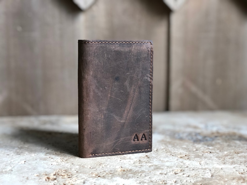 May include: A brown leather wallet with a stitched edge and the initials "AA" embossed on the front.