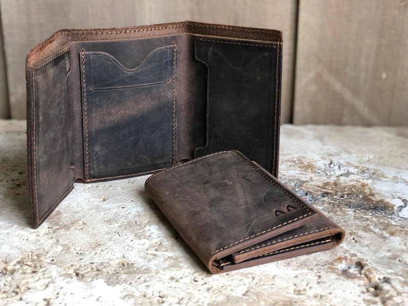 May include: Two brown leather wallets, one folded open to show the interior pockets and the other folded closed. The closed wallet has the initials "AA" embossed on the front.