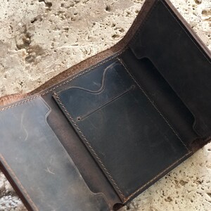May include: A brown leather wallet with multiple compartments and stitching details. The wallet is open and the interior is visible.