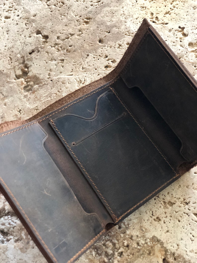 May include: A brown leather wallet with multiple compartments and stitching details. The wallet is open and the interior is visible.