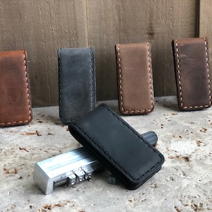 May include: Five leather money clips in different colors: brown, gray, brown, brown, and black. The clips are stitched with a contrasting thread.