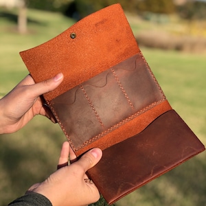 May include: A brown leather wallet with three card slots and a large pocket. The wallet is open and the inside is visible.