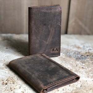 May include: Two brown leather wallets with a distressed finish. The wallet on top has the initials "AA" embossed on the front.