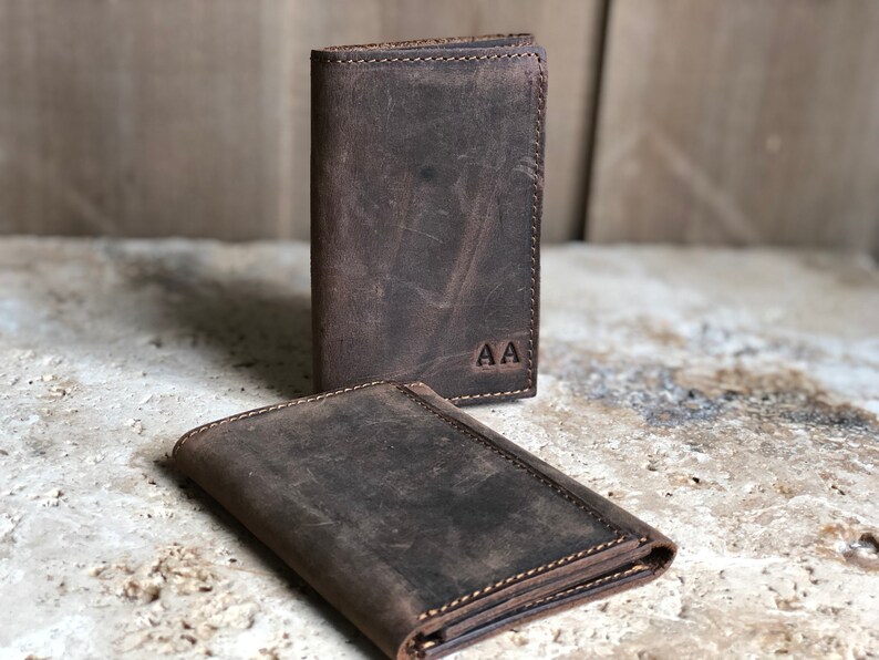 May include: Two brown leather wallets with a distressed finish. The wallet on top has the initials "AA" embossed on the front.