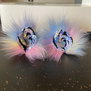 May include: A pair of colourful faux fur cat ears with iridescent sequin details. The ears are pink, blue and yellow.
