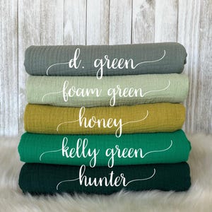 May include: A stack of five rolled fabric swatches in various shades of green and yellow. The colors are labeled with elegant cursive text: d. green, foam green, honey, kelly green, and hunter.