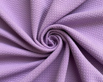 May include: A close-up of a soft, textured, lavender fabric. The fabric is folded and twisted, creating a swirling pattern.