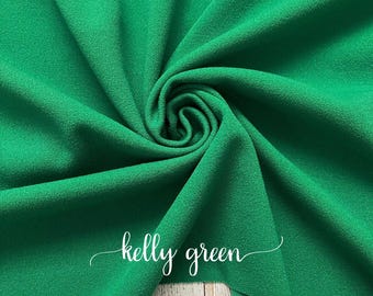 Puede incluir: Primer plano de una tela verde kelly con superficie texturizada. La tela está doblada y drapeada sobre una superficie de madera.