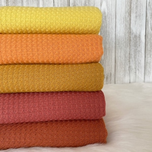 May include: A stack of five waffle weave fabric swatches in shades of yellow, orange, mustard, red, and rust.