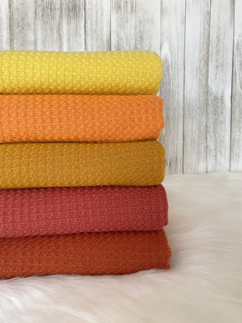 May include: A stack of five waffle weave fabric swatches in shades of yellow, orange, mustard, red, and rust.