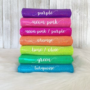 May include: A stack of seven different colored glittery fabrics, from top to bottom: purple, neon pink, neon pink/purple, orange, lime/olive, green, and turquoise. Each fabric has a white text label indicating its color.