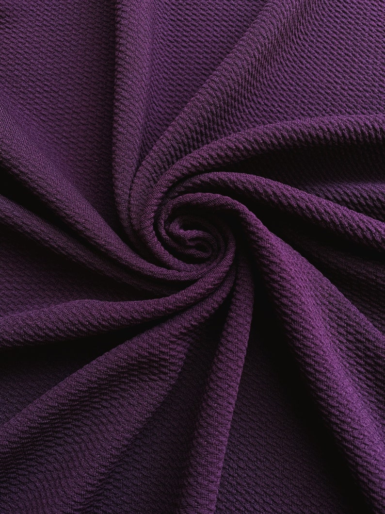 May include: Close-up of a deep purple textured fabric with a soft, crinkled appearance. The fabric is folded and twisted, creating a swirling pattern.