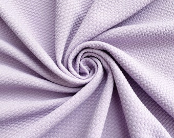 May include: A soft, textured, lavender-colored fabric with a waffle-like pattern. The fabric is folded and twisted into a spiral shape.