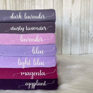 May include: A stack of seven fabric swatches in various shades of purple, pink, and red. The swatches are labeled with the following names: dark lavender, dusty lavender, lavender, lilac, light lilac, magenta, and eggplant.