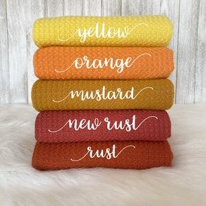 May include: Five waffle weave fabric swatches in shades of yellow, orange, mustard, new rust, and rust. The swatches are stacked on top of each other, with the yellow swatch on top and the rust swatch on the bottom.