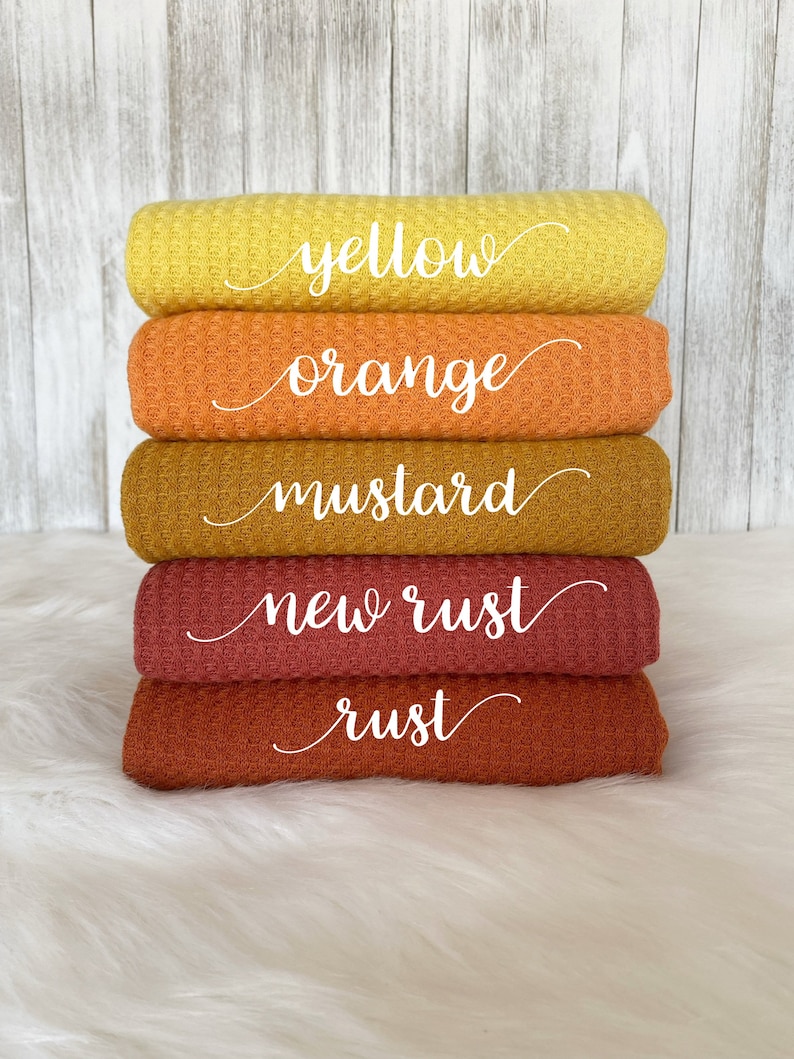 May include: Five waffle weave fabric swatches in shades of yellow, orange, mustard, new rust, and rust. The swatches are stacked on top of each other, with the yellow swatch on top and the rust swatch on the bottom.