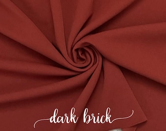 Puede incluir: Primer plano de una tela de color rojo ladrillo oscuro. La tela está doblada y retorcida, mostrando su textura. El texto "dark brick" está escrito en cursiva blanca sobre la tela.