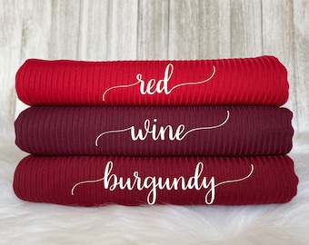 Peut inclure: Trois rouleaux de tissu côtelé dans des tons de rouge, bordeaux et vin. Le tissu est étiqueté "rouge", "vin" et "bordeaux".