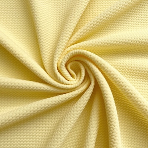 May include: A close-up of a yellow textured fabric. The fabric is folded and twisted, creating a swirling pattern.