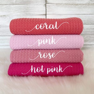 May include: Four waffle weave fabric swatches in shades of pink, coral, and rose. The swatches are stacked on top of each other, with the coral swatch on top and the rose swatch on the bottom. The swatches are labeled with the color names: coral, pink, rose, and hot pink.