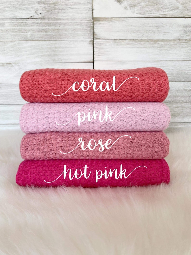 May include: Four waffle weave fabric swatches in shades of pink, coral, and rose. The swatches are stacked on top of each other, with the coral swatch on top and the rose swatch on the bottom. The swatches are labeled with the color names: coral, pink, rose, and hot pink.