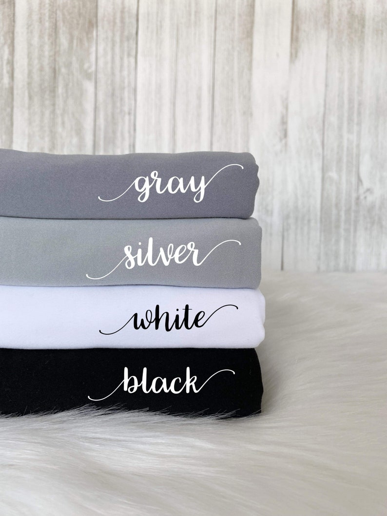 May include: Four fabric swatches stacked on top of each other. The swatches are gray, silver, white, and black. Each swatch has the color name written in white cursive on the fabric.