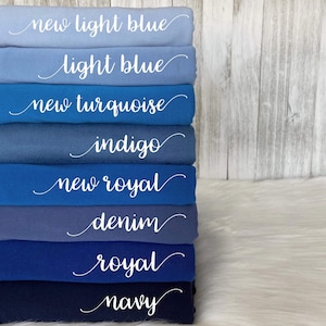 May include: A stack of folded fabric in various shades of blue, from light blue to navy. Each layer is labeled with a cursive white font, indicating the color name: "new light blue", "light blue", "new turquoise", "indigo", "new royal", "denim", "royal", and "navy".