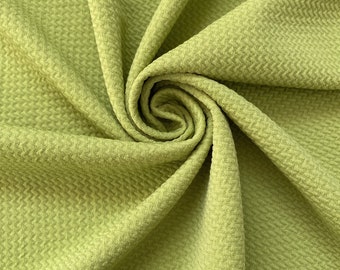 May include: A close-up of a textured, green fabric. The fabric is folded and twisted, creating a swirling pattern.