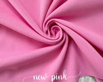 Puede incluir: Un primer plano de una tela suave y rosa con una ligera textura. La tela está doblada y retorcida, creando un patrón de espiral. Las palabras "new pink" están escritas en cursiva blanca sobre la tela.
