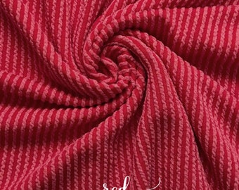 May include: Red ribbed fabric with a textured pattern. The fabric is folded and the word "red" is written on it.