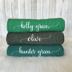 May include: Three rolls of ribbed fabric in shades of green. The top roll is kelly green, the middle roll is olive, and the bottom roll is hunter green.