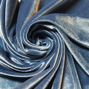 May include: Close-up of a soft, blue velvet fabric with a subtle sheen. The fabric is folded and twisted, creating a swirling pattern.
