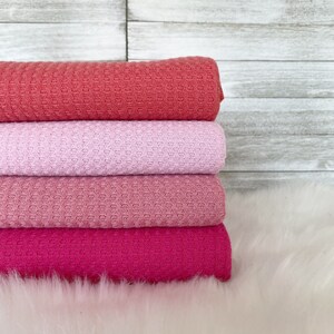 May include: Four waffle weave fabric swatches stacked on top of each other. The swatches are in shades of pink, coral, and red.
