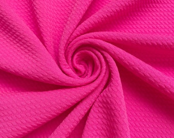 May include: Close-up of a bright pink fabric with a textured waffle-like pattern. The fabric is folded and draped, creating a soft and inviting look.