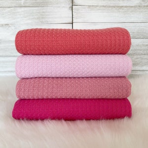 May include: Stack of four waffle weave fabric swatches in shades of pink, coral, and fuchsia.