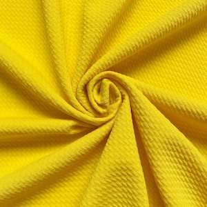 May include: A close-up of a bright yellow fabric with a textured waffle weave pattern. The fabric is folded and draped, creating a soft and inviting look.