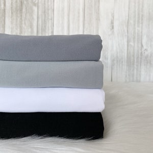 May include: Four pieces of fabric stacked on top of each other. The top piece is a light gray, the second piece is a darker gray, the third piece is white, and the bottom piece is black.