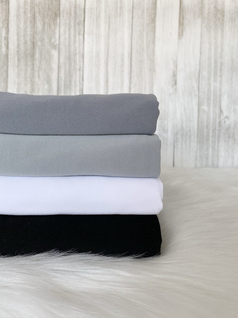 May include: Four pieces of fabric stacked on top of each other. The top piece is a light gray, the second piece is a darker gray, the third piece is white, and the bottom piece is black.