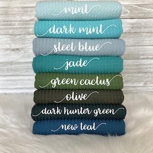 May include: A stack of eight waffle weave fabric swatches in various shades of blue and green. The swatches are labeled from top to bottom: mint, dark mint, steel blue, jade, green cactus, olive, dark hunter green, and new teal.
