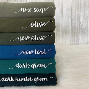 May include: Stack of six fabric swatches in various shades of green and teal. The swatches are labeled with the names "new sage", "olive", "new olive", "new teal", "dark green", and "dark hunter green".