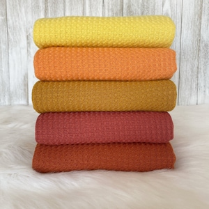 May include: A stack of five waffle knit fabric swatches in shades of yellow, orange, brown, red, and rust.