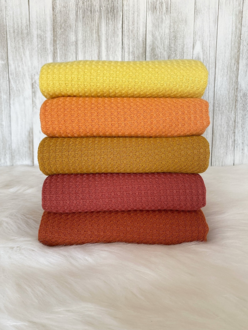May include: A stack of five waffle knit fabric swatches in shades of yellow, orange, brown, red, and rust.