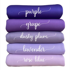 May include: A stack of five fabric rolls in shades of purple, with the names of the colors written in cursive script. The colors range from a deep purple to a light rose lilac. The names of the colors are purple, grape, dusty plum, lavender, and rose lilac.